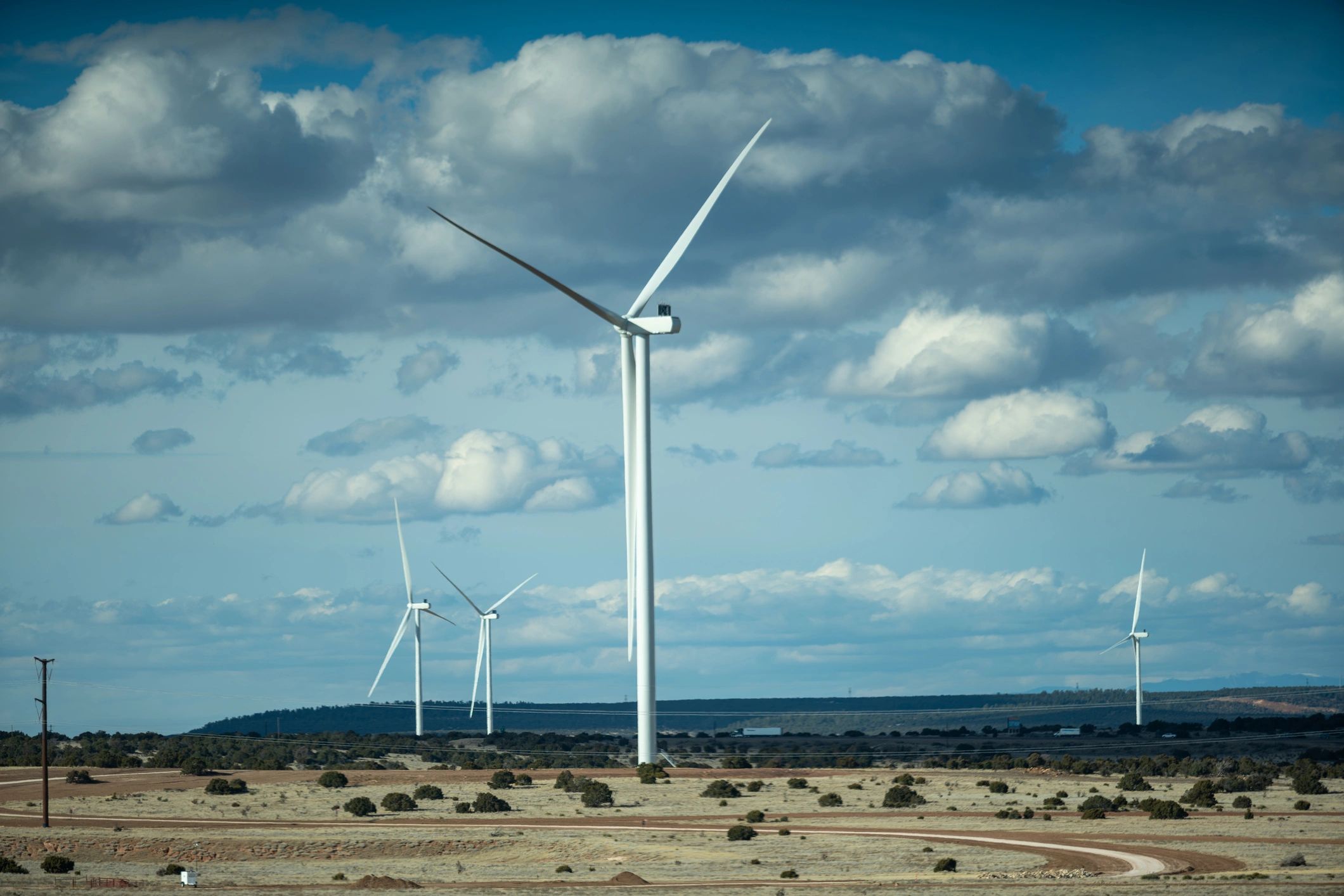 Wind turbines generating renewable energy across high desert landscape. Multiple modern turbines operating in arid terrain under partly cloudy sky.